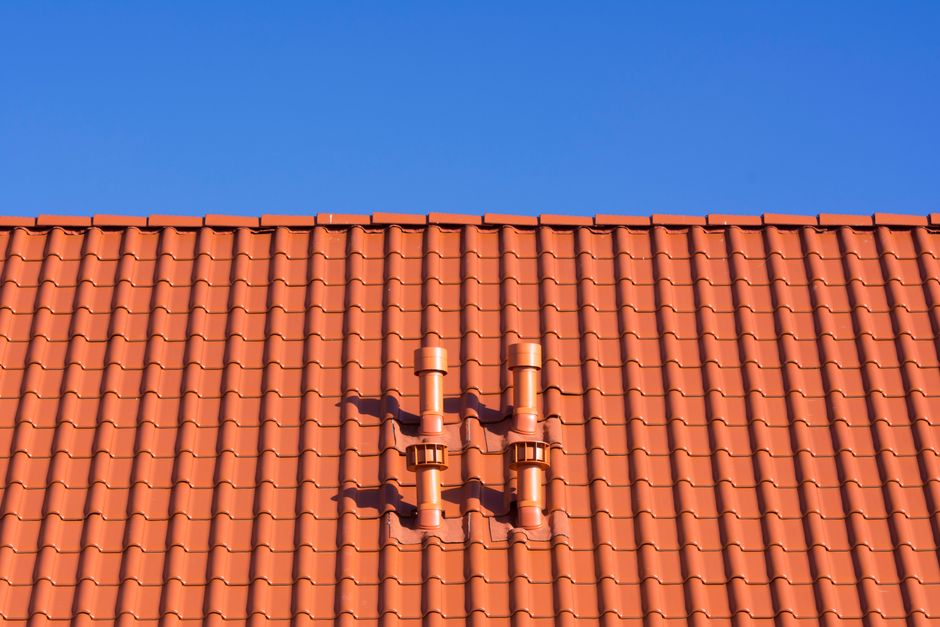 Orange clay tile roof with chimneys against blue sky showing professional installation